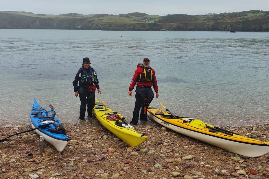 A group of people standing next to kayaks on a beach Description automatically generated with low confidence