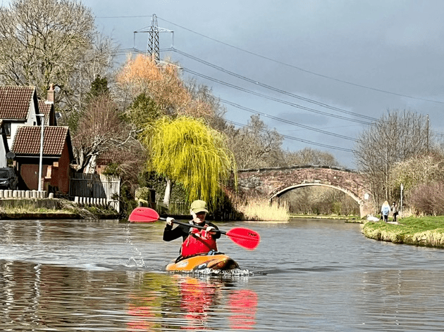 A person in a kayak in a river with a bridge in the background Description automatically generated with medium confidence