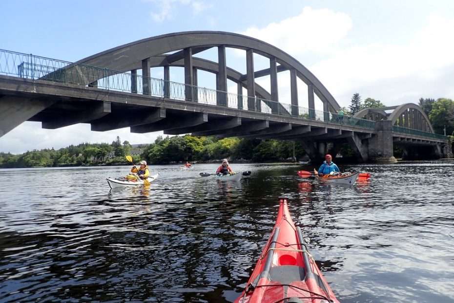 A group of people kayaking under a bridge Description automatically generated